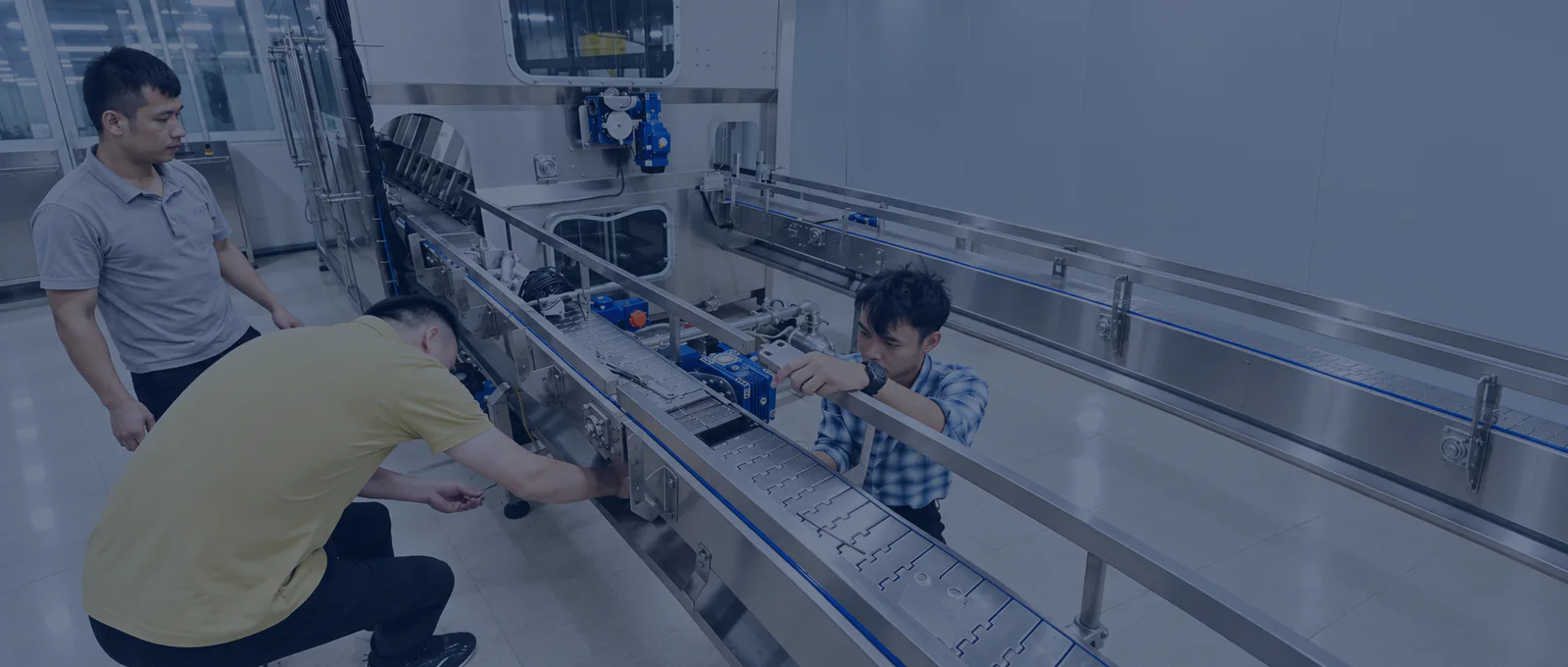 Three technicians installing and commissioning a stainless-steel beverage conveyor at the customer site
