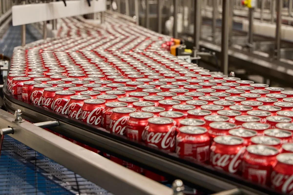 Red Coca-Cola cans moving along a stainless-steel beverage production conveyor