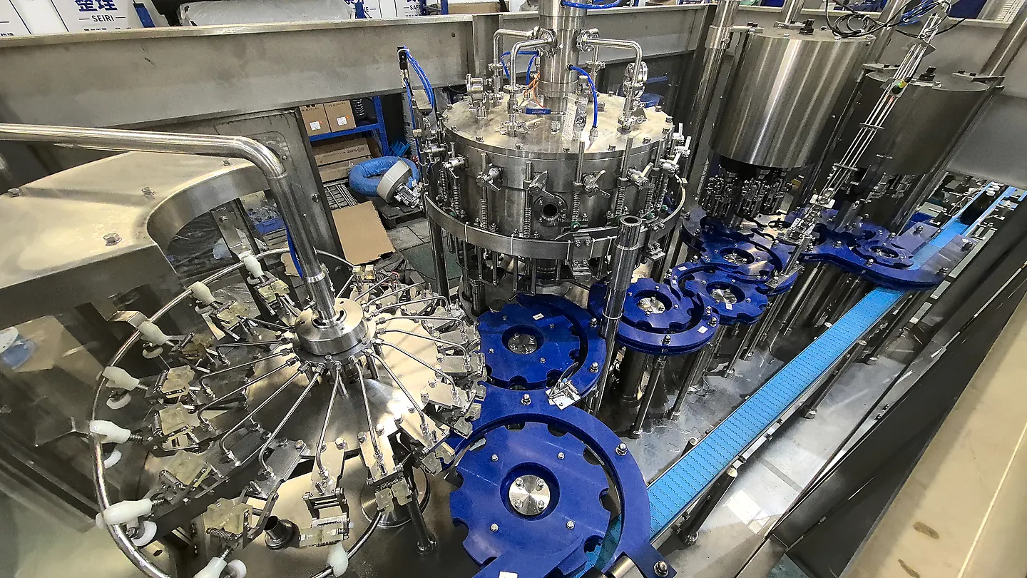 Top view of integrated glass bottle rinsing, counter-pressure filling and closing stations with blue transfer starwheels