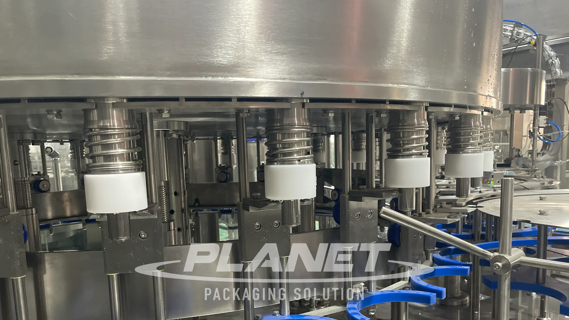 Large PET water bottles positioned beneath stainless-steel filling valves